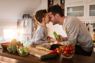 Child and man with faces press together in affection while preparing food