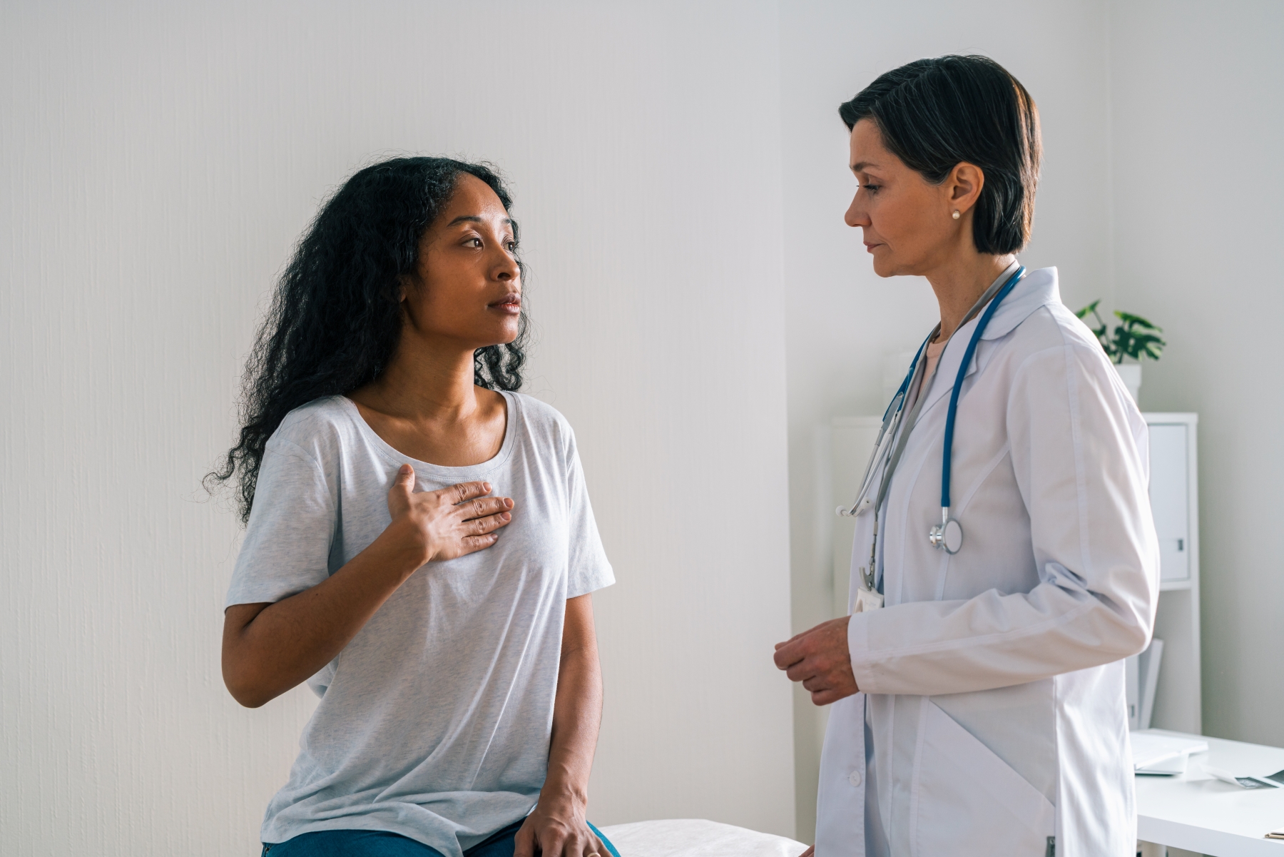 A young woman puts hand to her heart as she talks with a female doctor.
