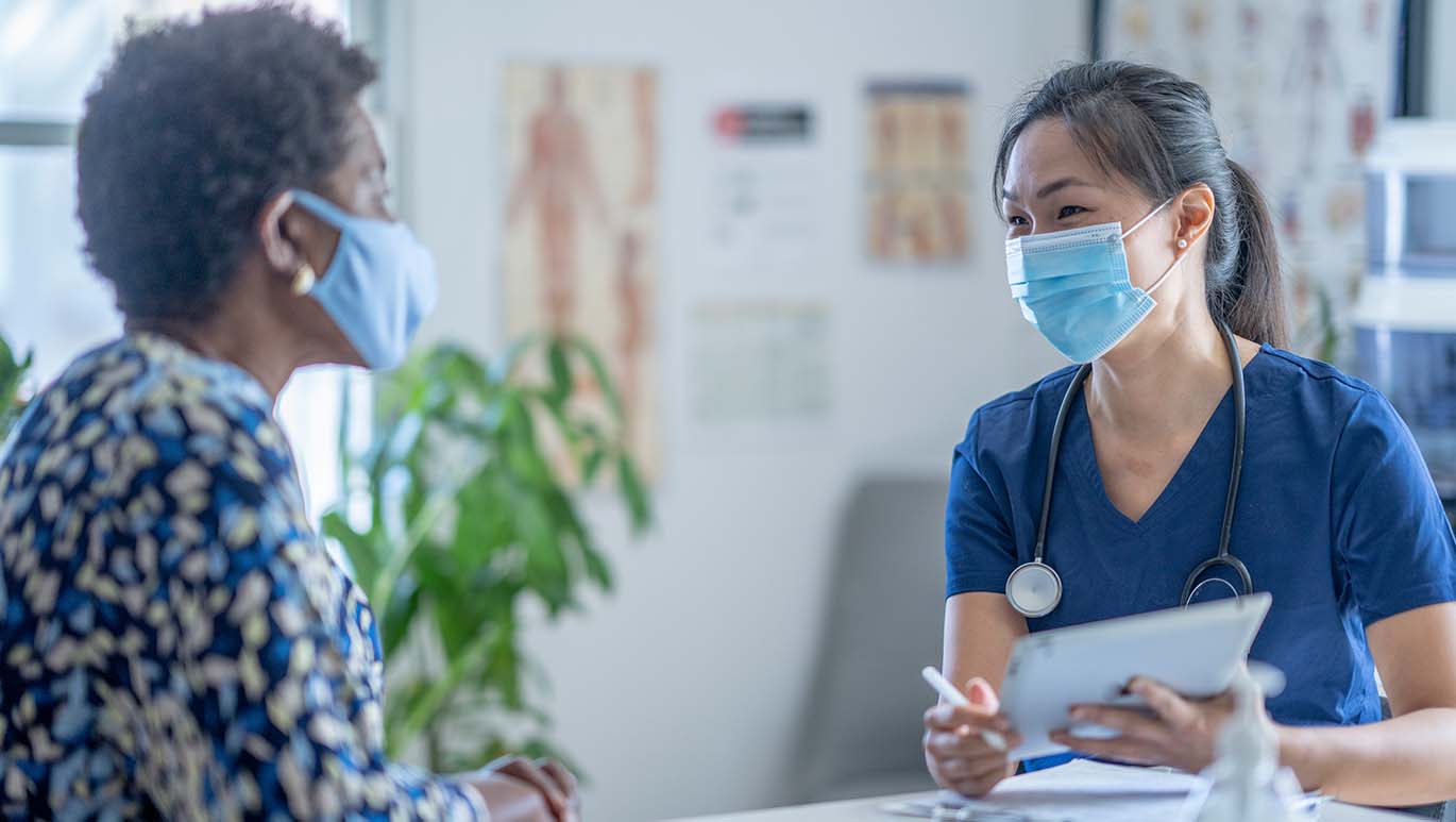 Female nurse and patient wearing PPE and discussing medical paperwork