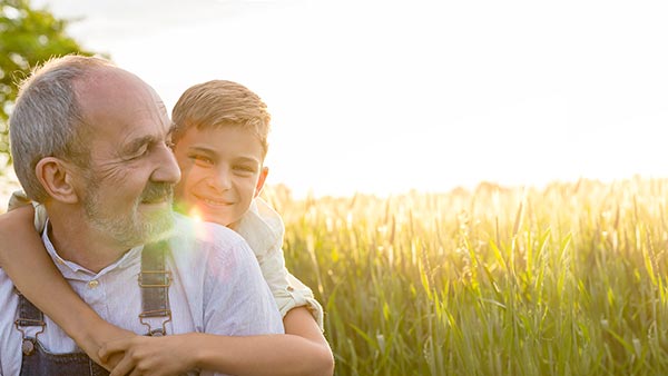 Older man giving a child a piggyback ride in a field.