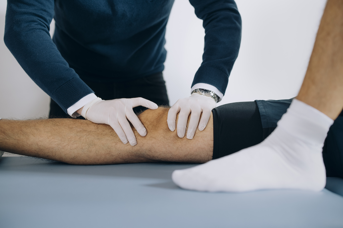 A physical therapist examines and manipulates a patient's knee during a therapy session