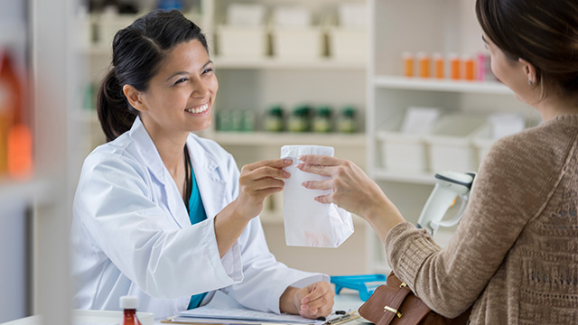 A person handing over a package at a pharmacy counter.
