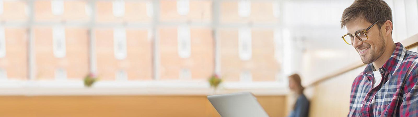 A man sitting in a bright, modern setting, smiling and looking at his laptop.