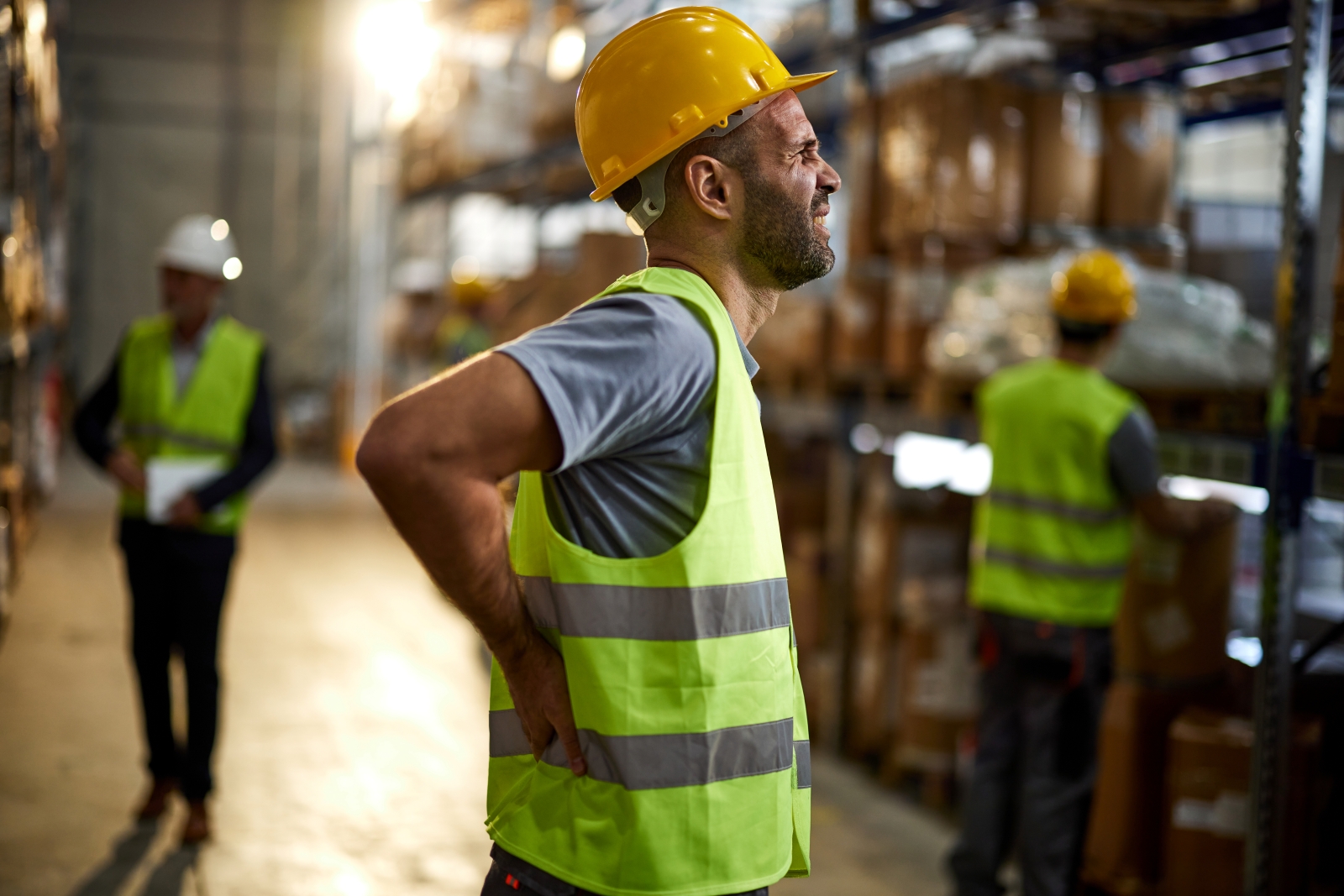 man in hard hat and safety vest holding back in pain