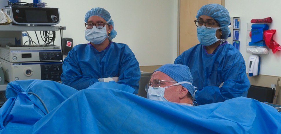 Team wearing scrubs performing procedure on patient covered in drapes